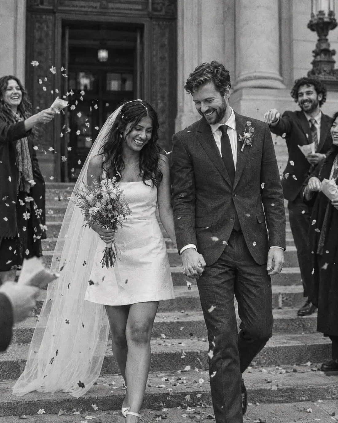 Black and white: the couple walk down the city hall steps hand in hand while friends throw petals.